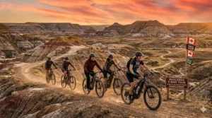 A photorealistic 4K detailed photograph of a diverse group of five friends on a multi-rider trail e-bike tour, including the male rider from image_14 and the woman from image_0, navigating the multi-colored badlands formations near Drumheller, Alberta, under a spectacular golden sunset.