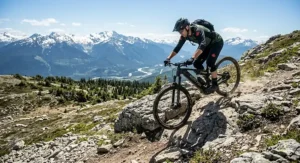 A cyclist riding a 150mm travel trail ebike through vibrant autumn leaves on a technical Quebec trail.
