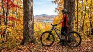 Alt text for image 6: A versatile lightweight hardtail electric mountain bike being ridden along a paved waterfront cycling path in Toronto, with the iconic city skyline and CN Tower visible under a clear blue sky.